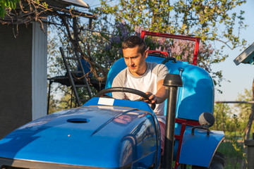 Young man in t-shirt driving tractor with sprayer