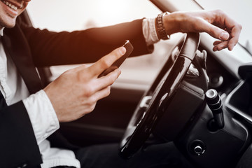 Naklejka premium Smiling young man is holding mobile phone in car
