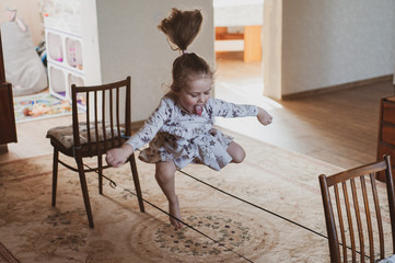 A happy girl jumps through an elastic band strung between chairs. Idea for quarantined child activity