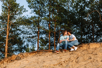 Naklejka na ściany i meble Lovers sit on a sandy cliff against the background of a forest