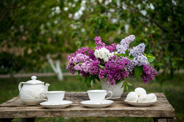 Lilac spring flowers in vase on wooden background. Tea coffee cup on table during breakfast time