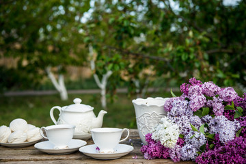 Lilac spring flowers in vase on wooden background. Tea coffee cup on table during breakfast time