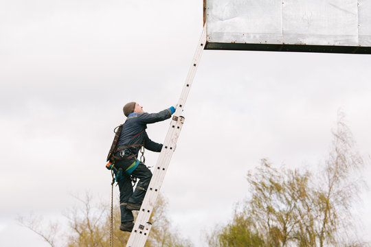 Industrial climber going up the ladder to the billboard. Risky job. Work on height