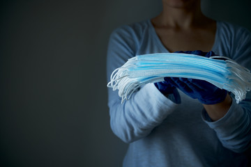 A woman holds a stack of face protective medical masks in latex disposable gloves on a dark background, close-up. Save lives.