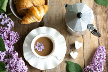 Coffee break. Bouquet of lilac with a cup of latte. Lilac in the girl on the desktop. Wooden old table with coffee. First coffee, then business. The concept of romance. Spring. Coffee maker