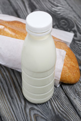 Bottle of milk and ciabatta bread in a package. On brushed pine boards.