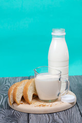 Bottle of milk, a glass of fermented baked milk and slices of ciabatta bread on a cutting board. On brushed pine boards.