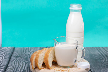 Bottle of milk, a glass of fermented baked milk and slices of ciabatta bread on a cutting board. On brushed pine boards.