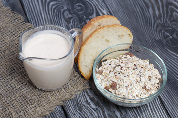 Glass with milk. Nearby in a muesli container. Sliced Ciabatta. On brushed pine boards.