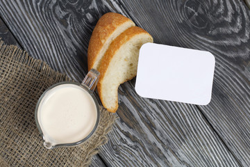 Glass with milk. Next to slices of ciabatta and cottage cheese. On brushed pine boards.
