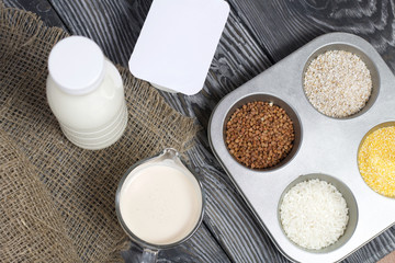 Bottle and glass with milk. Near the cottage cheese and a container with cereals: buckwheat, rice, barley and corn. On brushed pine boards.