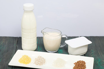 Bottle and glass with milk. Near the cottage cheese and a container with cereals: buckwheat, rice, barley and corn. On brushed pine boards.