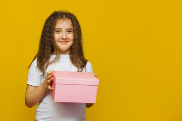Fototapeta premium Little cute girl holding gift box on Yellow background.