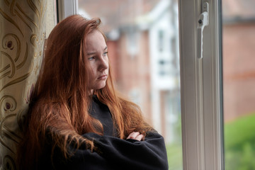 Upset teenage girl during quarantine at home looking out window