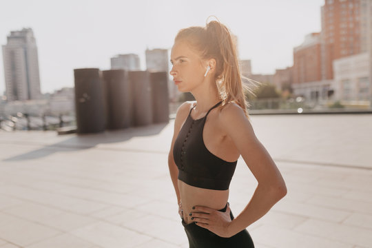 Fashionable sportswoman, training, healthy lifestyle. Adorable athletic woman training in morning sunlight with headphones in the city