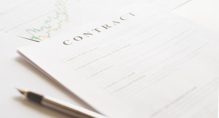 Contract paper and pen on white desk background. Focus on title Contract. Defocused pencil.