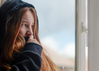 Depressed teenager girl looking out window at home