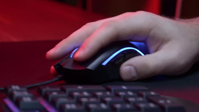 A gamer is playing in a computer club. In the frame, the hand of a gamer and a gaming mouse. Red and violet colors. ESports competitions.


