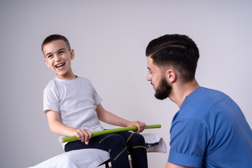 The boy lies on a special table, next to him is a doctor in blue uniform and he helps the guy to do physical exercises, rehabilitation concept