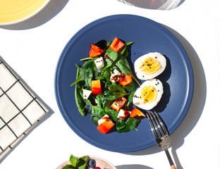 Healthy sunny morning breakfast on the white table. Salad with spinach, red pepper, feta cheese eggs with boiled eggs. Top view