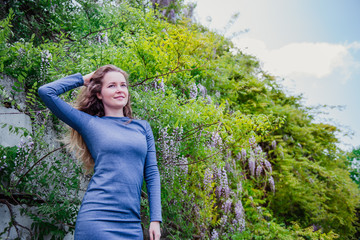 Naklejka premium Beautiful girl in a blue dress on the background of a flowering Wisteria tree