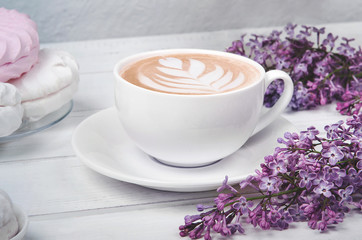 Obraz na płótnie Canvas Lilac, coffee cup with latte art and marshmallow on white wooden table. Flat lay