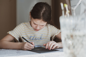 A teenager girl draws using the technique of scratching with a sharp tool of paper, drenched with...