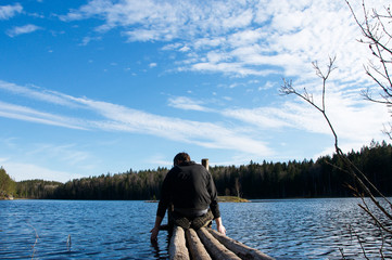 Man sitting  at looking at lake in forest. People and nature concept. Outdoor activity. Recreation concept. Lake in forest. Old wooden pier. People from behind 