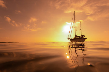 Yacht sailing against golden sunset.