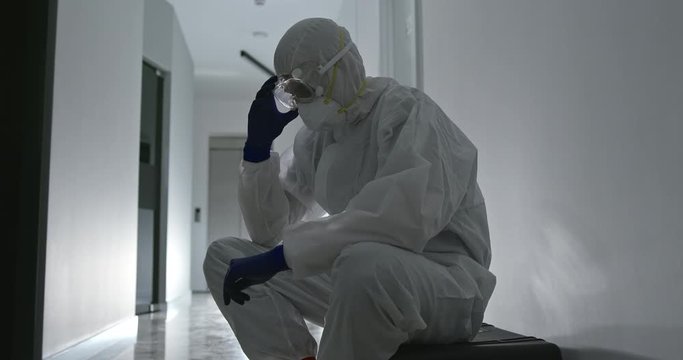 Tired male health worker with face bruises take off protective uniform after overwork with patients COVID 19 infected and then resting in corridor of modern hospital