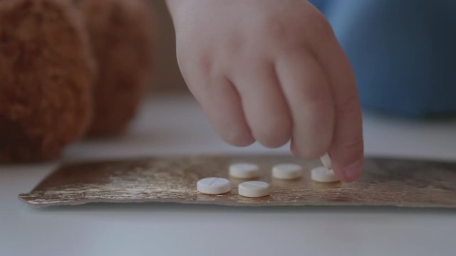 Kid plays with scattering medicine drugs. Toddler touches pills without parent control. Dangerous situation.