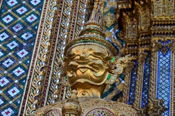 Fototapeta na wymiar Golden guardian in front of a wall of mosaics at Wat Phra Kaew in Bangkok