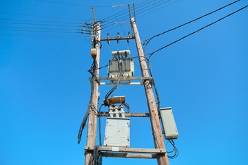 Electric transformer on wooden poles, blue sky background