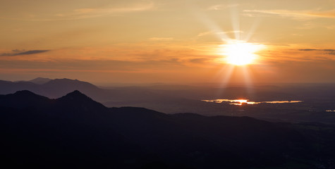 Lake Staffelsee from mountain peak Jochberg during sunset with sun, mountain silhouettes of the Bavarian Alps, Bavaria Germany.
