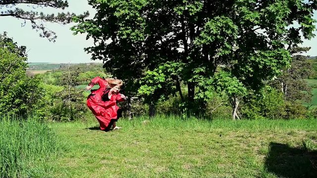 Lady in red running falling down in red dress escaping in nature in historic costume