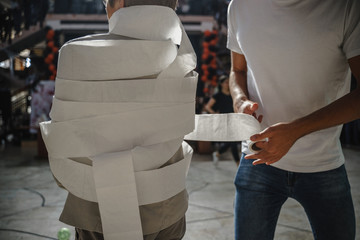 Short old woman being wrapped in toilet paper in a Halloweeen Game by a Tall young man