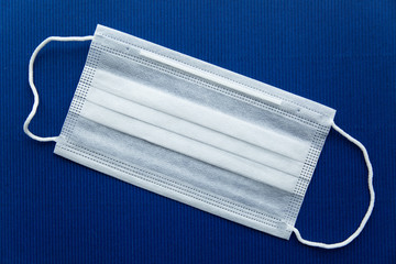 one white protective mask on a dark blue background diagonally close-up. Personal protective equipment