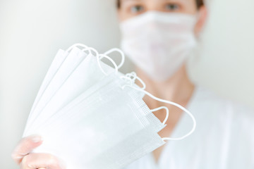 White protective medical masks in hand in the foreground ,a woman with a mask in the background in the center.