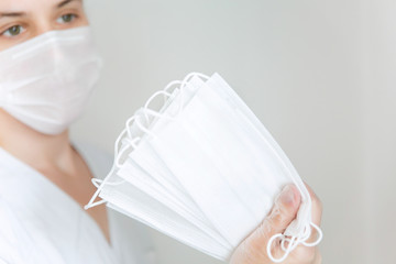 White protective medical masks in hand in the foreground ,a woman with a mask in the background on the left.