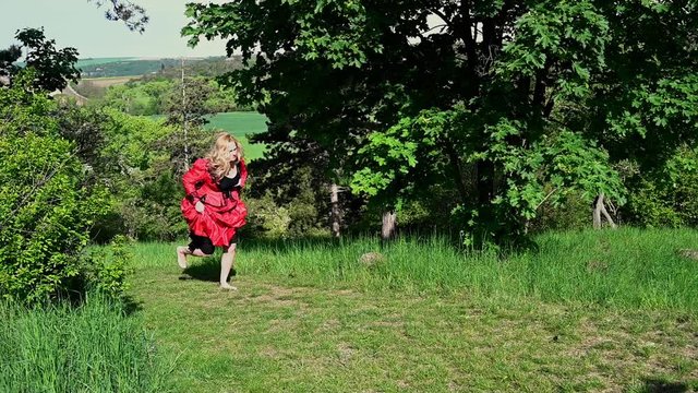 Blond woman running in red historical costume dress in nature. Excaping.