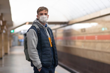 Young guy man, in a protective medical mask, against the background of the subway, tunnel, Waiting for a train. Epidemic concept, pandemic virus