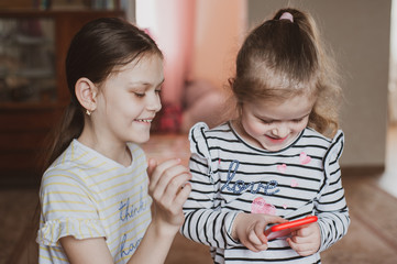 Happy little girls with a smartphone in hands communicate at home with loved ones using modern technology