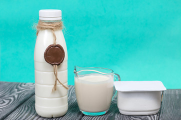 Bottle of milk. On the neck of the bottle is twine with a wax locket. Near a glass of ryazhenka and cottage cheese. On brushed pine boards.