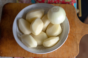 Raw peeled potatoes and peeled onions in a plate