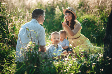 Fototapeta premium dad and mom with young children are sitting on the grass on a picnic and laughing