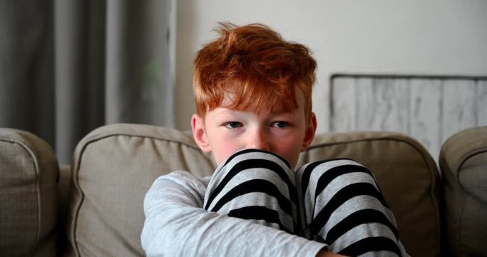 Reddish boy with red hair sitting on sofa sad watching tv alone 