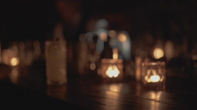 Close up shot of a bar counter in a bar in Bangkok, Thailand. Human drinks a cocktail, candles are burning in the background.