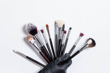Professional makeup brushes isolated on white background. Hand in a black glove holds a set of professional brushes for cosmetics on a white background. Copy space for text. Makeup. Brushes.