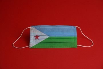 Coronavirus protective mask. Medical mask combined with the Djibouti flag. Red background. Face mask protection against pollution, virus, flu. Healthcare and surgery concept.