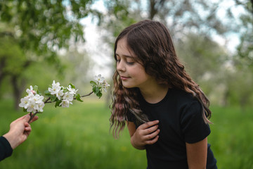 Tender brunette girl in black t-shirt leaned towards blooming branch in boy's hand